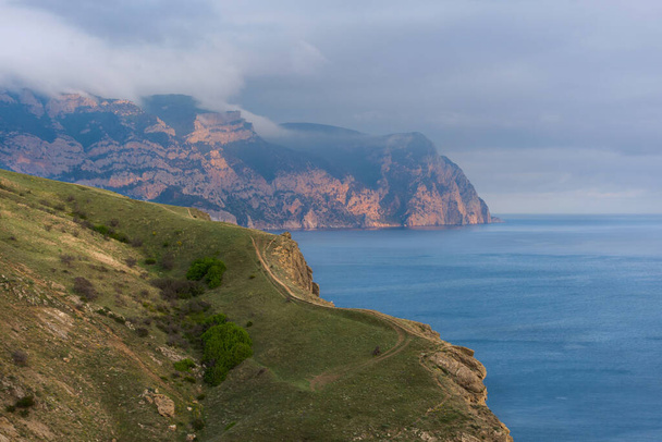 Cape ay-ya Crimea Balaklava. Sea coast and mountains with clouds. Beautiful landscape at sunset. Low clouds over the mountain. path along the sea. - Foto, Imagem