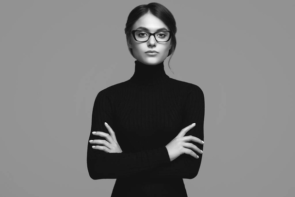 Portrait of cute student girl wearing black turtleneck sweater and stylish eyeglasses posing on gray background in studio - Photo, Image