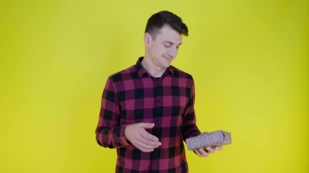 Handsome man throws box with gift from hand to hand on yellow background - Кадры, видео