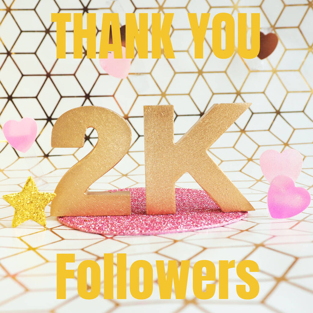 Lettrage en lettres volumétriques dorées "Thank you 2K followers" et coeurs en plastique rose sur fond géométrique blanc et or. - Photo, image