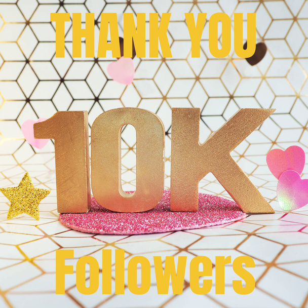 Lettrage en lettres volumétriques dorées "Thank you 1K followers" et coeurs en plastique rose sur fond géométrique blanc et or. - Photo, image