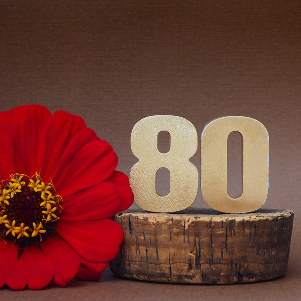 80 dígitos dourados volumétricos e flor de gerbera vermelha em um fundo marrom. espaço para texto
 - Foto, Imagem