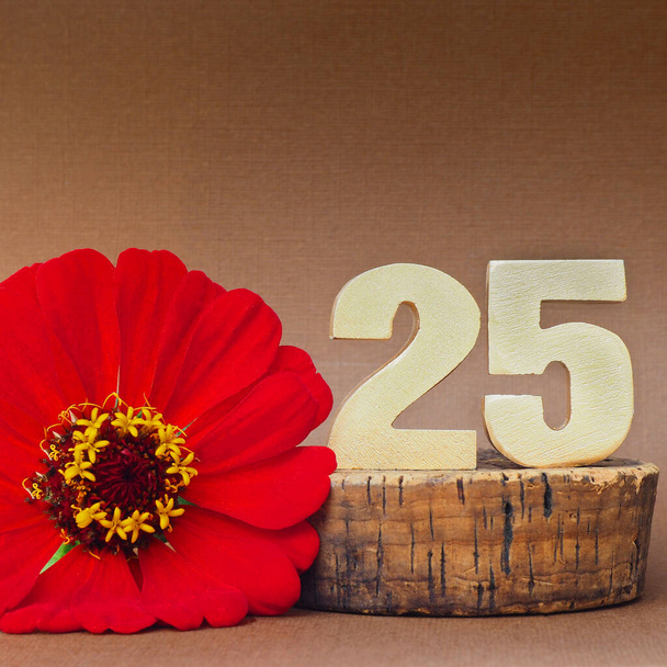 Χρυσός ογκομετρικός αριθμός "25" και ένα κόκκινο λουλούδι ζέρμπερα σε καφέ φόντο. τόπος για κείμενο - Φωτογραφία, εικόνα