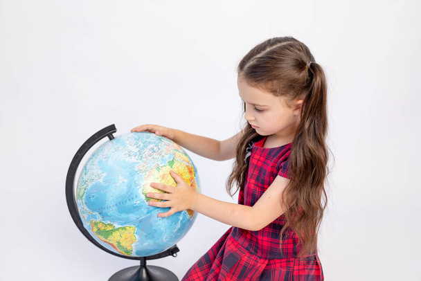 little girl school girl 7 years old sitting in a red dress with a globe on a white isolated background, place for text, September 1, knowledge Day - Foto, Imagen