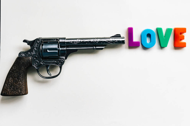 Hračková pistole s dětskými písmeny před hlavní tvořící slovo láskyKontrastní myšlenky nebo pojmy, síla a násilí proti lásce - Fotografie, Obrázek