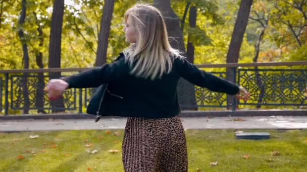 Onnellinen nainen musta takki, leopardi hame kävelee puistossa, pyörii onnea - Materiaali, video