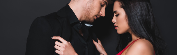 panoramic shot of sexy woman touching shirt of handsome man isolated on black  - 写真・画像