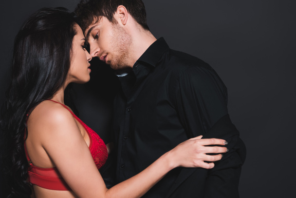 side view of sexy woman in red bra touching shirt of handsome man on black  - Fotó, kép