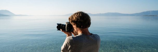 Genç erkek fotoğrafçının sabah denizinin kenarında duran güzel yaz manzarasının fotoğraflarını çektiği geniş bir manzara.. - Fotoğraf, Görsel
