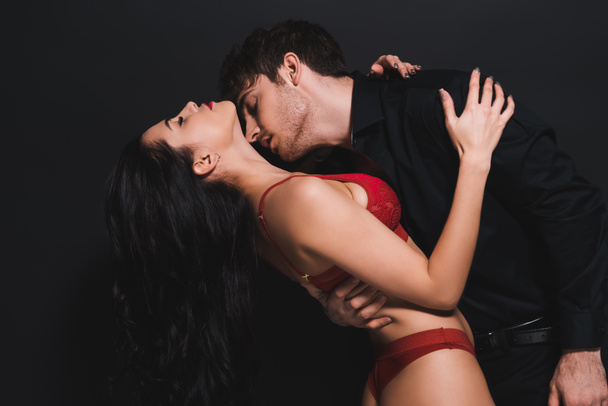szenvedélyes férfi csók nyak csábító nő piros melltartó elszigetelt fekete - Fotó, kép