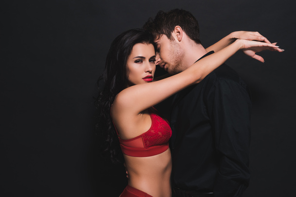 sexy woman in red bra and panties hugging handsome man isolated on black  - Foto, afbeelding