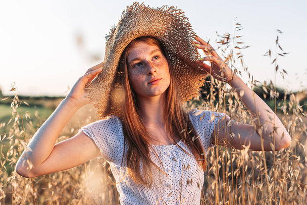 Portrait of young, teen, ginger girl with freckles in the wheat field wearing a summer hat - Foto, immagini
