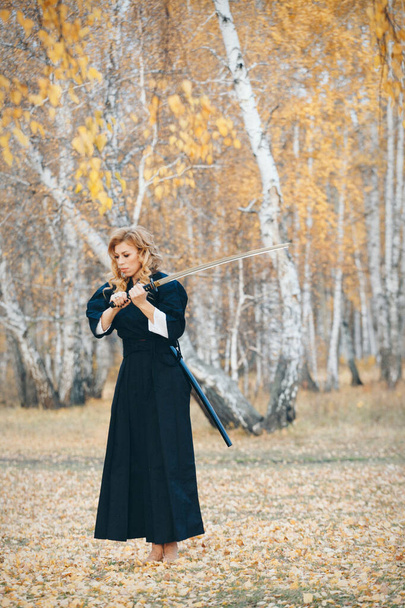 European woman with a katana in a kimono. the girl trains martial arts. a woman in the autumn forest. a warrior with a cold weapon in his hands - Фото, зображення