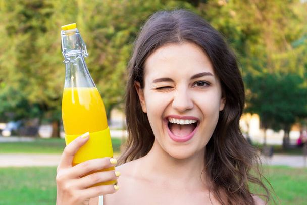 Menina está andando no parque segurando uma garrafa de suco frio fresco ou limonada em um dia ensolarado quente
. - Foto, Imagem