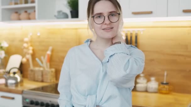 Loving happy European appearance of woman mother of an African girl hurries to feed her breakfast in kitchen at home. Portrait of smiling young stylish girl wearing glasses and shirt looking at camera - Imágenes, Vídeo