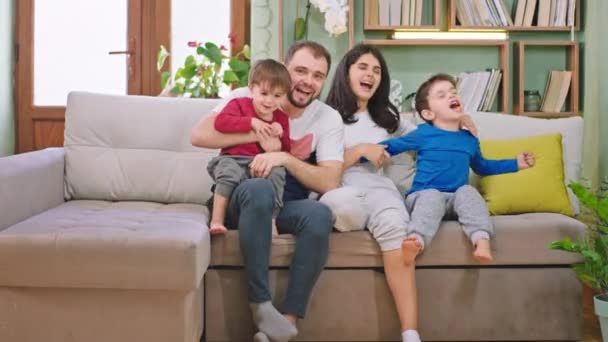 Happy family time on the sofa with a large smile two kids and parents watching something on the tv they laughed and enjoying the time in front of the camera - Imágenes, Vídeo