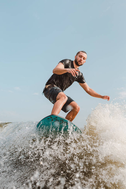スポーツマンがボートの後ろのサーフボードトレイルをサーフィンしています。川の夏のレジャーでのウェイクサーフィン - 写真・画像