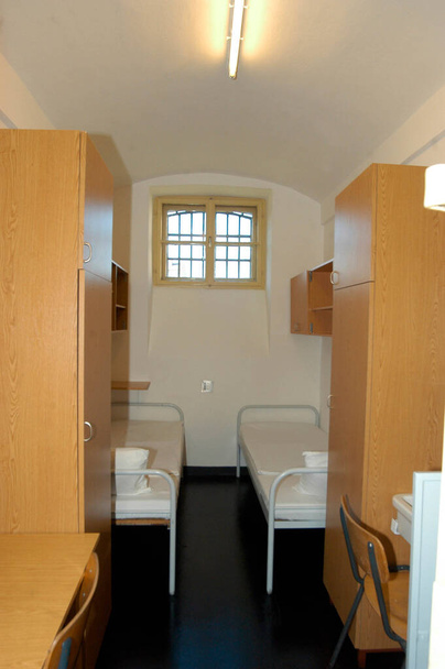 wewnątrz celi więziennej z dwoma łóżkami, szafami, biurkami i krzesłami - Zdjęcie, obraz