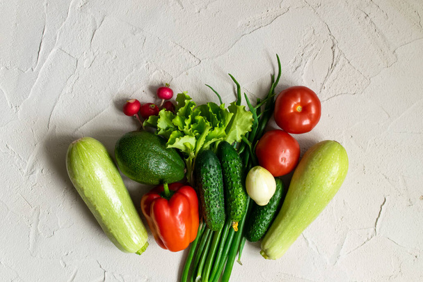 Assortment of fresh green red organic vegetables. zucchini, cucumber, onion, avocado, lettuce, pepper, tomatoes and radish on a concrete background. flat lay - Foto, Imagen