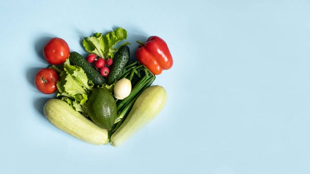 Σύνθεση φρέσκων πράσινων κόκκινων βιολογικών λαχανικών. κολοκυθάκια, αγγούρι, κρεμμύδι, αβοκάντο, μαρούλι, πιπέρι, ντομάτες και ραπανάκια σε μπλε φόντο. επίπεδο lay, αντίγραφο χώρου - Φωτογραφία, εικόνα