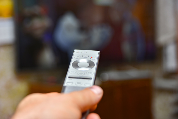 Um homem tem um controle remoto na mão e muda de canal para assistir TV. Controle remoto de eletrodomésticos
 - Foto, Imagem