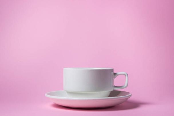 Біла чашка на рожевому фоні. Порожня біла порцелянова чашка на блюдці
. - Фото, зображення