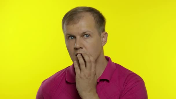 Egy fiatal fehér férfi portréja rózsaszín pólóban. Aggódó jóképű srác megdöbbent, fél, fél - Felvétel, videó