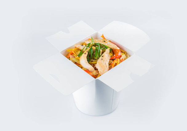 Izolované asijské nudle s kuřecím řízečkem, zeleninou, sójovou omáčkou a jarními cibulovými hřebenatkami v krabičce z bílého kartonu. Balíček s jídlem připraveným k jídlu uvnitř - Fotografie, Obrázek