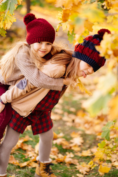 two girls in hats are playing and having fun in autumn park. - Zdjęcie, obraz