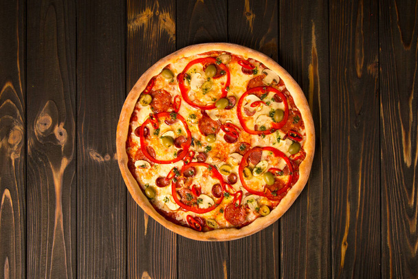 Top näkymä pizza paprika, vihreät oliivit, savustettu makkarat, mozzarella juusto, pepperoni, salami, chili pippuri, herkkusieniä puinen tausta. Maukasta leikkaamatonta pizzaa. Pikaruoka herkullinen astia - Valokuva, kuva
