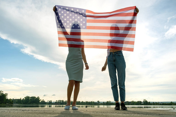 Siluetti kaksi nuorta ystävää naiset pitävät Yhdysvaltain lippu käsissään seisoo yhdessä ulkona. Isänmaalliset tytöt juhlivat Yhdysvaltain itsenäisyyspäivää. - Valokuva, kuva