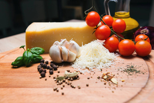 Parmesan cheese on a wooden board and cherry tomatoes, olive oil, onions, garlic, spices. - Fotó, kép