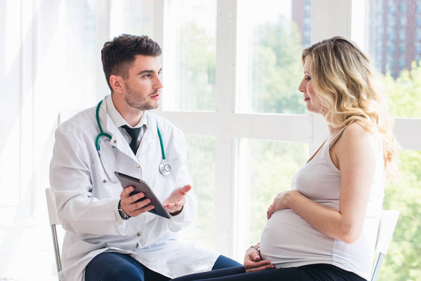 Pregnant woman visiting young doctor - Фото, изображение