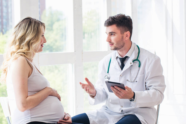 Pregnant woman visiting young doctor - 写真・画像