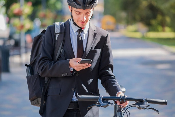 Male bicycle commuter in a suit and helmet with a phone. Cycling around the city, going to office work by bike - Foto, Bild