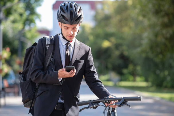Portrait of a male commuter in a suit and bicycle helmet with a phone. Cycling around the city, going to office work by bike - Fotó, kép