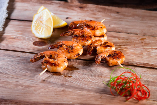 Appetizing fried shrimp on a skewer on a wooden surface among lemon and seasonings. The concept of fast and wholesome food - Photo, Image