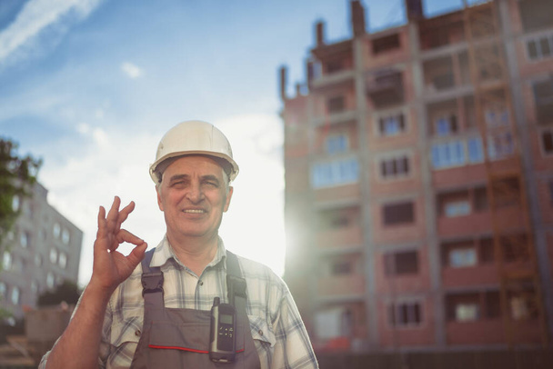 Senior engineer smiling broadly showing up gesture ok to camera, expression of like and approval. Sunset time - 写真・画像