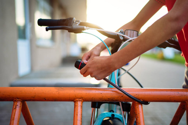 Girl teenager fastening bicycle lock on street parking at sunset - Фото, изображение