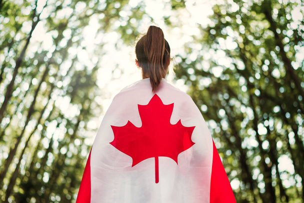 Child teenager girl at nature background an Canada flag on her shoulders   - Фото, изображение