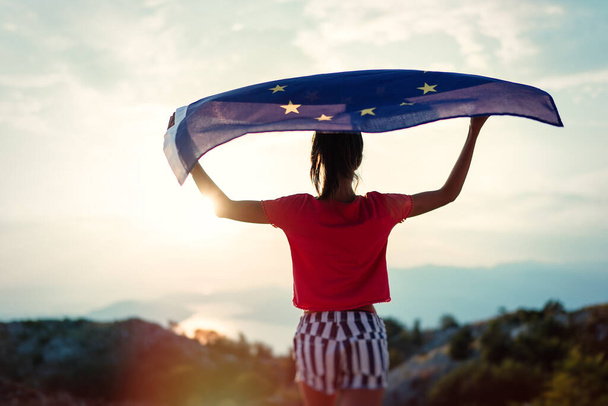 Child girl teenager young person is waving European Union flag on top of mountain at sky background. Sunset time - Photo, Image