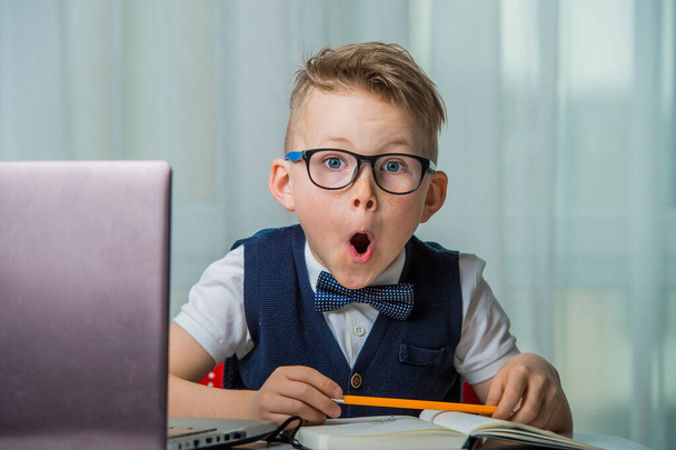 Funny geek kid in glasses using his laptop. Shocked surprised child react on news. Online education for pupil. - Photo, Image