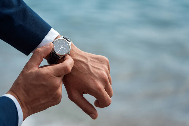 A man in a business suit checking a wrist watch on his hand on background  sea - Fotografie, Obrázek
