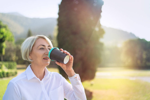 Mature woman drink takeaway coffee while resting at the park  - Foto, Imagen