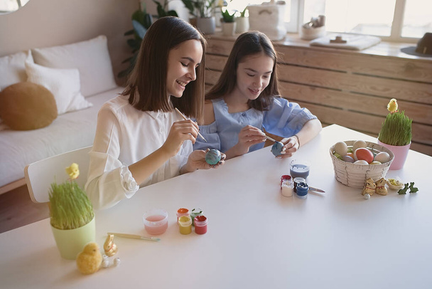                                Glückliche Teenager-Freundinnen bemalen zu Hause Eier mit Farben und Pinsel. Ostern, Feiertage und Menschen-Konzept        - Foto, Bild