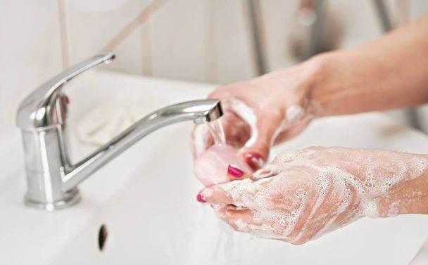 Nuori nainen pesee kätensä vesihanan alla saippualla. Tiedot suds peitetty iho. Henkilökohtainen hygienia käsite - sepelvaltimovirus covid-19 taudinpurkauksen ehkäisy - Valokuva, kuva