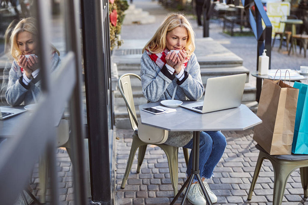 Attractive smiling female wearing grey coat looking to the screen laptop - Fotografie, Obrázek