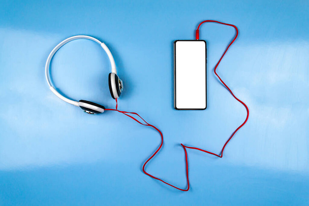 Mobile phone and white headphones. Blue background - Фото, изображение