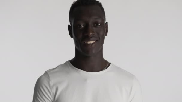 Schöner afroamerikanischer Typ im weißen T-Shirt, der vor grauem Hintergrund glücklich in die Kamera schaut - Filmmaterial, Video