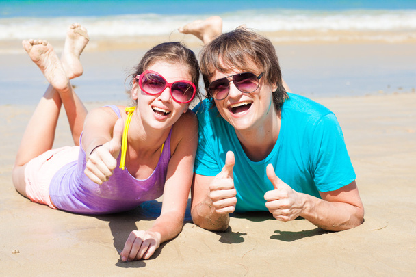 Close-up van gelukkige jonge paar in zonnebril liggend op het strand glimlachen - Foto, afbeelding